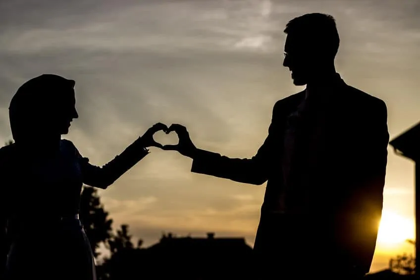 A Muslim couple touching hands and making a heart shape.