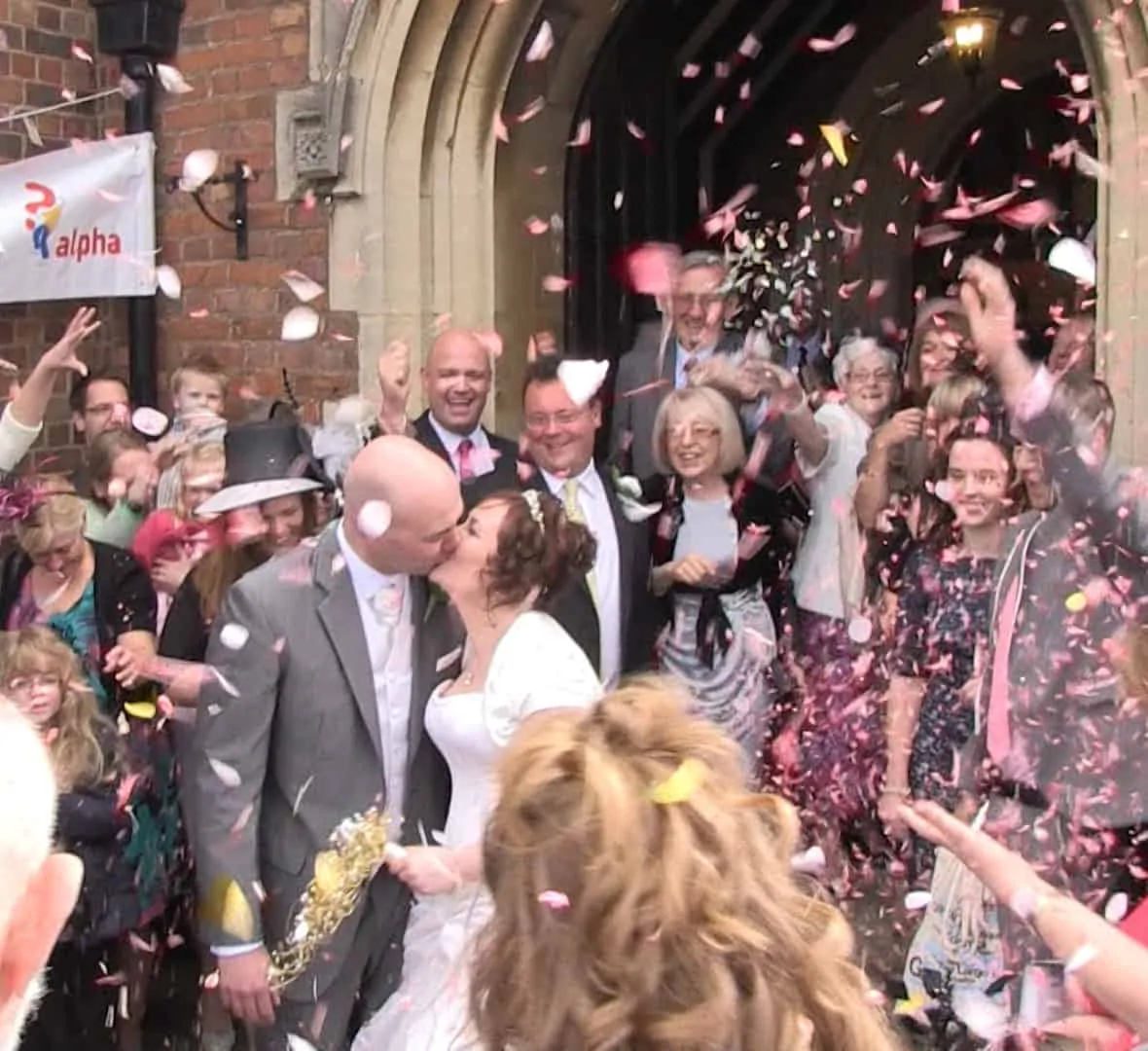 A newly wedded couple leaving the church. Confetti is being thrown by the crowd that surrounds them.