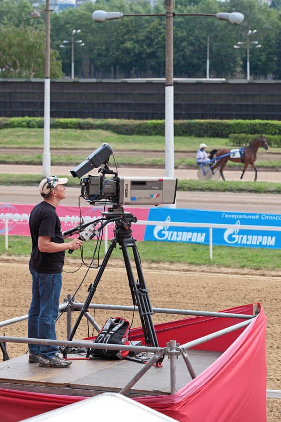 Why Your Existing Camera Company Has to Start Live Streaming A camera man with a camera designed for outdoor broadcasting at a horse racing related event.