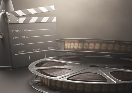 How Much Does Video Production Cost and Why? Two film reels in the foreground with a clapper board in the background.