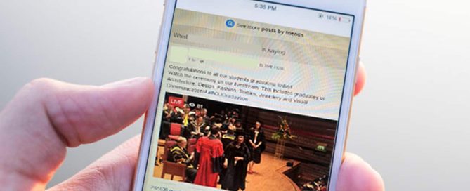 A mobile phone in a users hand. The phone screen shows a popular social media site.