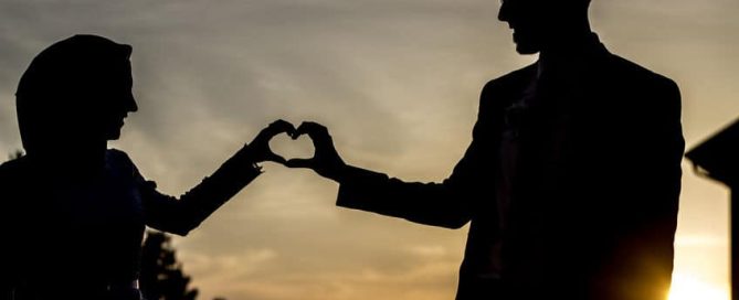 A Muslim couple touching hands and making a heart shape.