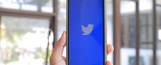 View of a mobile phone held in a hand with the Twitter logo displayed