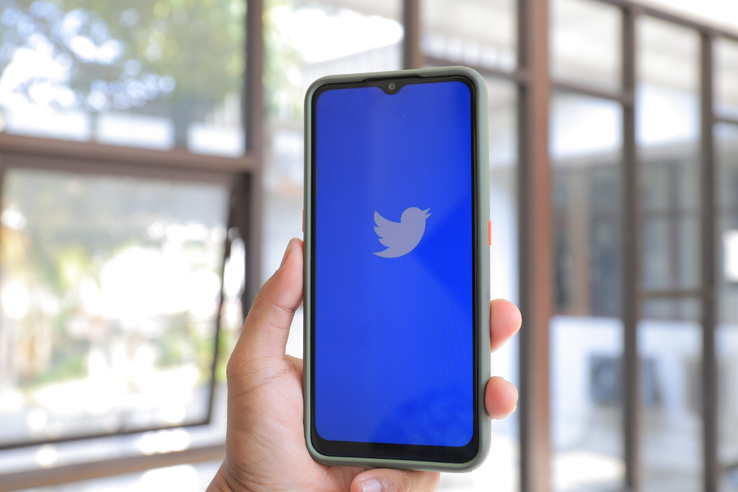 Twitter socials blog View of a mobile phone held in a hand with the Twitter logo displayed