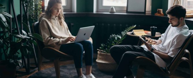 Two young people sat in their chairs working with a laptop and a tablet.